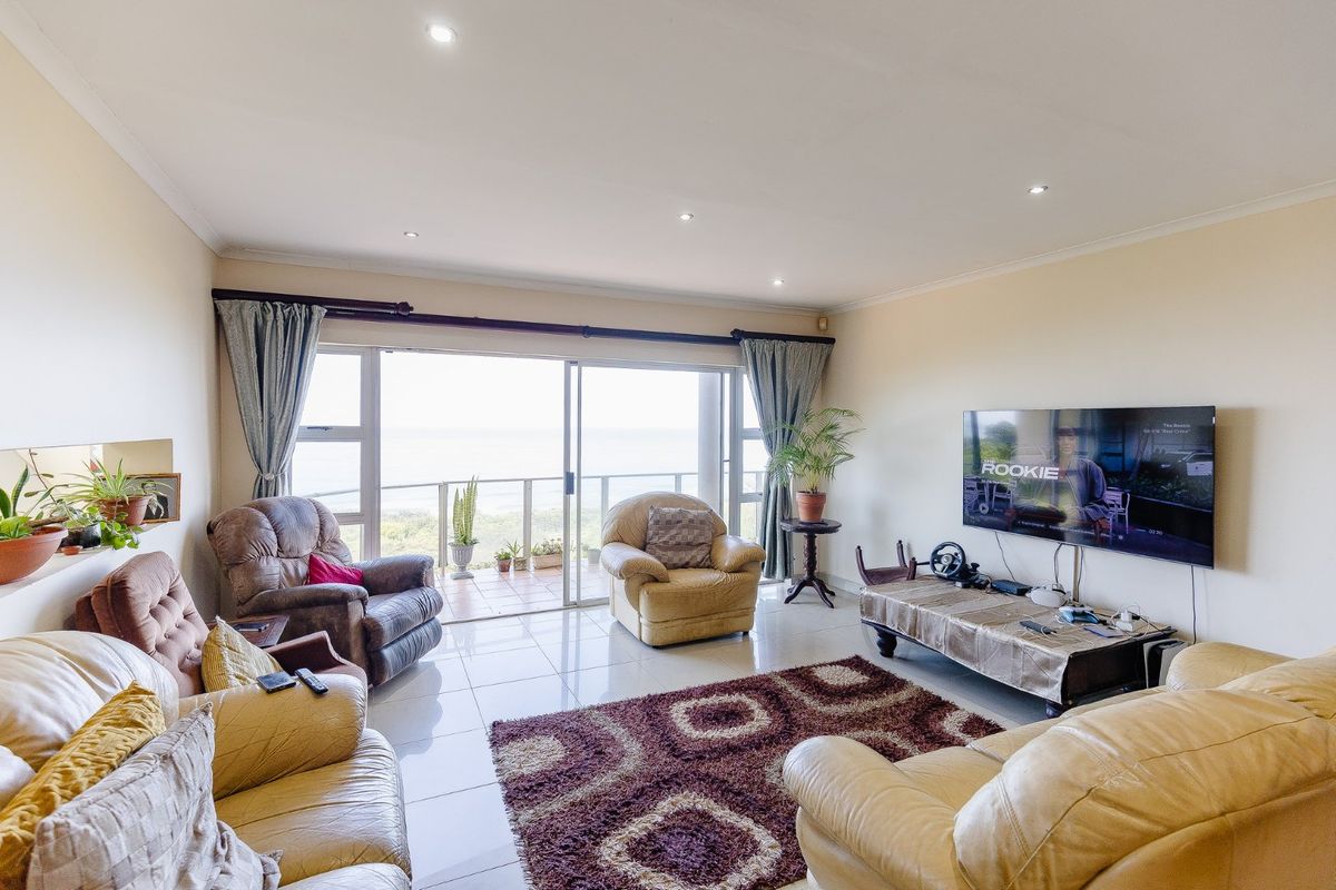 Spacious living room featuring large sliding glass doors that open onto a balcony with ocean views and bright tiled flooring.