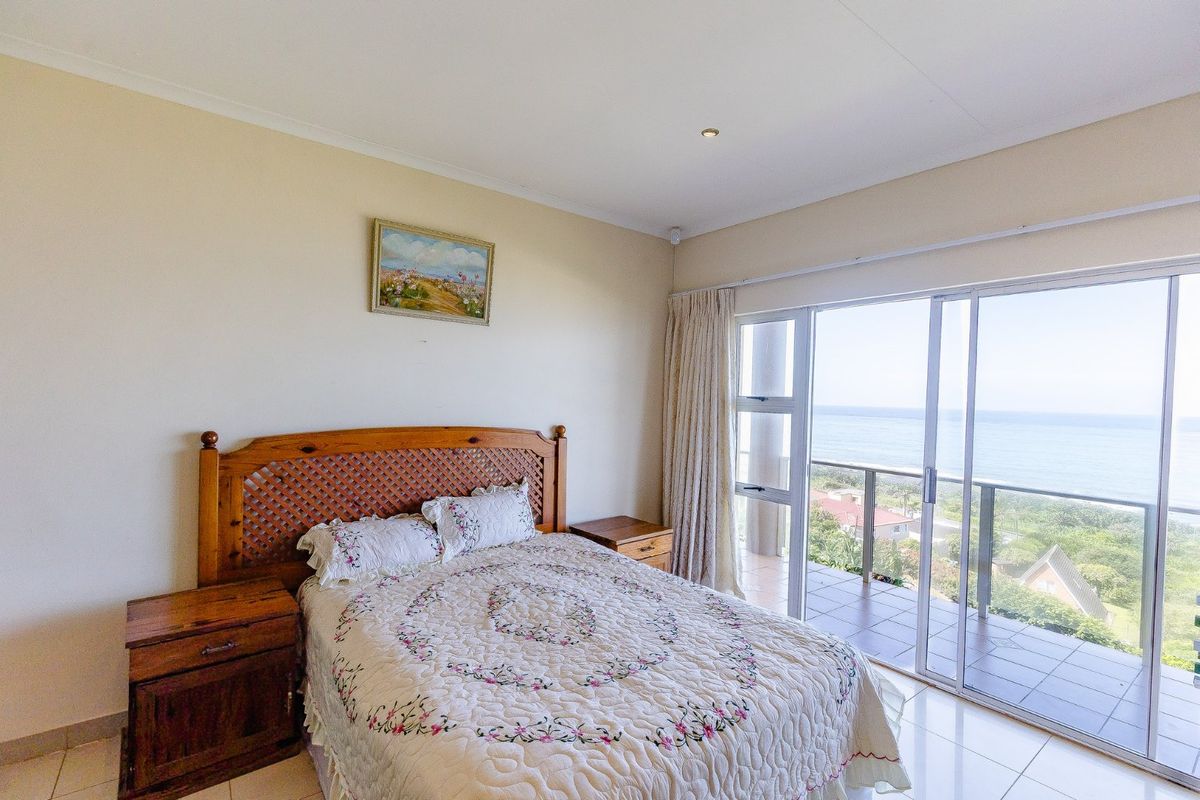 Spacious bedroom featuring tiled flooring, recessed lighting, and large sliding glass doors opening onto a balcony with scenic ocean views.
