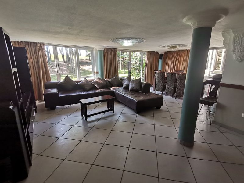 Spacious open-plan living and dining area featuring tiled flooring, structural columns, and large sliding glass doors providing natural light and garden access.