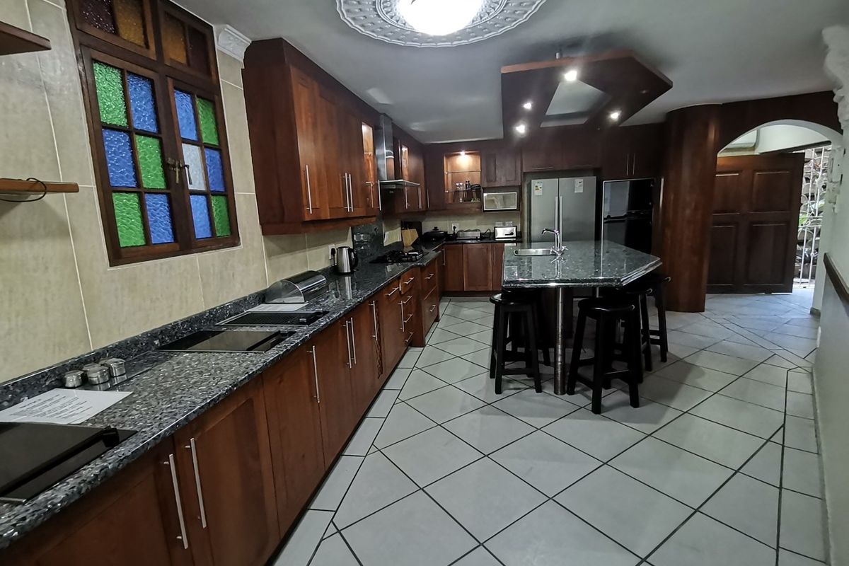 Spacious kitchen featuring dark wood cabinetry, granite countertops, a central island with seating, and unique stained glass window detailing.