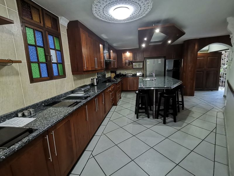 Spacious kitchen featuring dark wood cabinetry, granite countertops, a central island with seating, and unique stained glass window detailing.