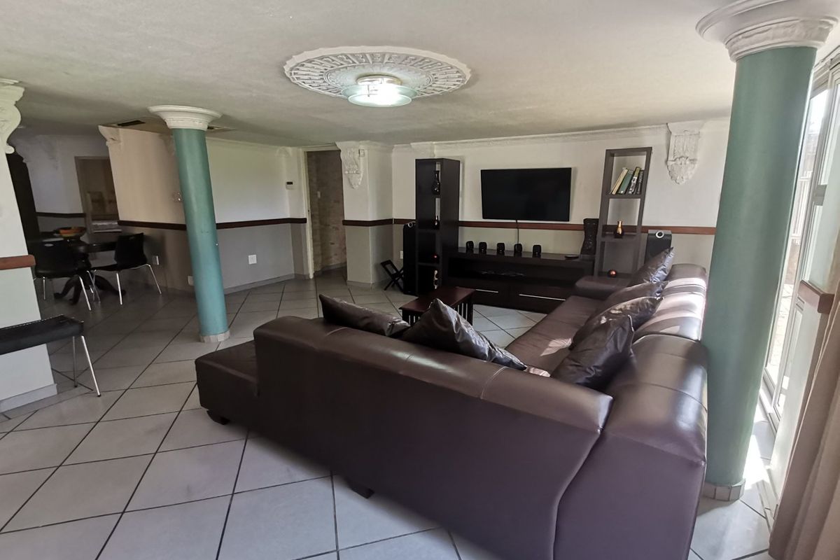 Spacious living area featuring tiled flooring, decorative ceiling detailing, and structural columns, offering a versatile layout for comfortable seating and entertainment.