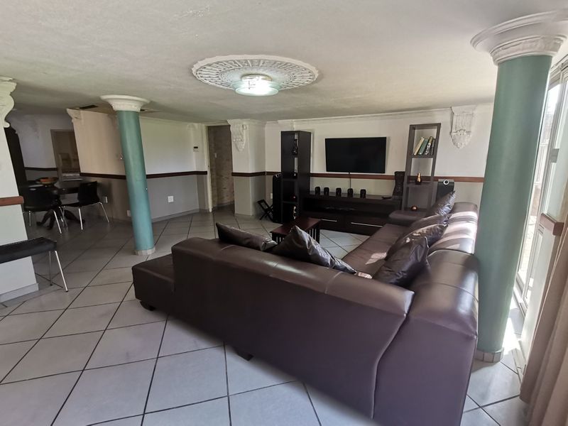 Spacious living area featuring tiled flooring, decorative ceiling detailing, and structural columns, offering a versatile layout for comfortable seating and entertainment.