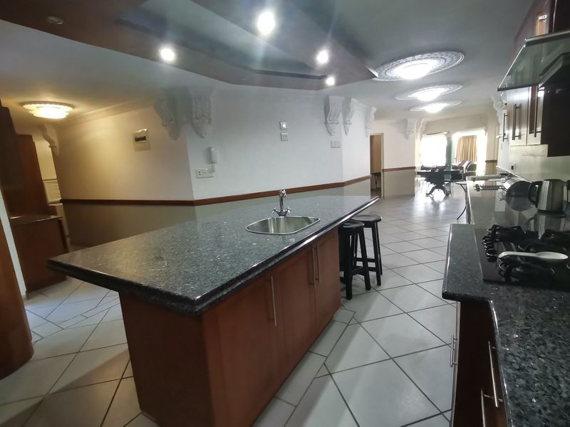 Spacious open-plan kitchen and living area featuring a large island with granite countertops, gas hob, and decorative ceiling details.