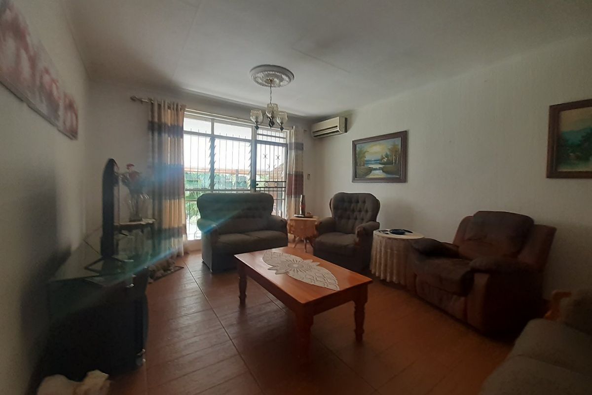 A living room featuring tiled flooring, a ceiling rose, and a wall-mounted air conditioning unit, with security bars installed on the window.