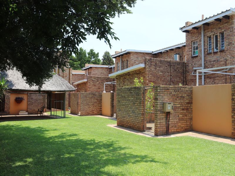 Rear view of a commercial property complex featuring face brick buildings, a thatched roof structure, and well-maintained lawn areas with secure boundary walls.