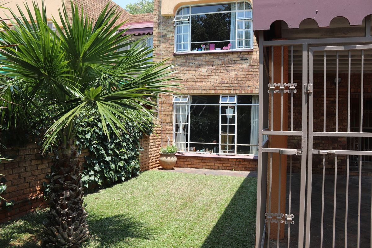 A rear view of the property featuring a face brick facade, steel-framed windows, a small lawn area, and a secure metal gate.