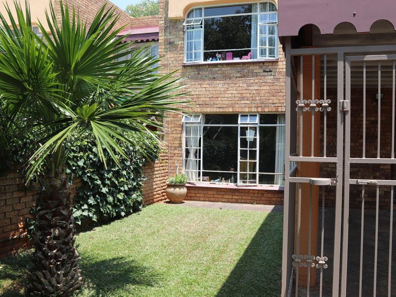 A rear view of the property featuring a face brick facade, steel-framed windows, a small lawn area, and a secure metal gate.