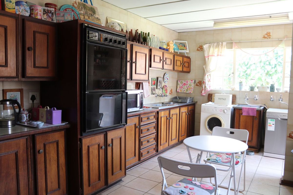 A dated kitchen featuring traditional wooden cabinetry, a double wall oven, tiled backsplash, and functional laundry plumbing connections.