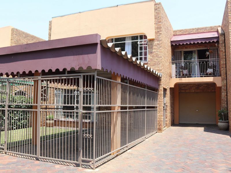 Front exterior view of a commercial property featuring a paved driveway, secure metal enclosure, roller garage door, and a balcony with metal railing.