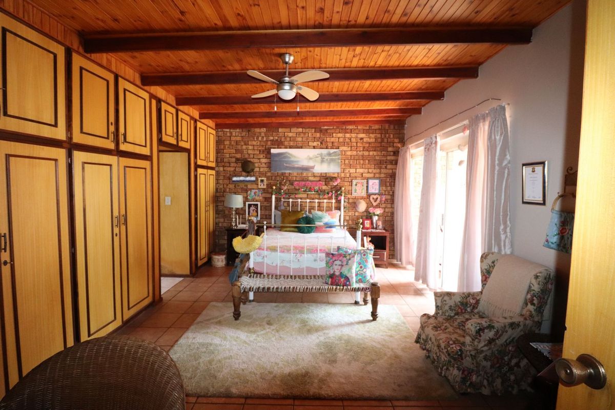Spacious bedroom featuring an exposed brick wall, timber beam ceiling, extensive built-in cabinetry, and direct access to the outdoors via sliding glass doors.
