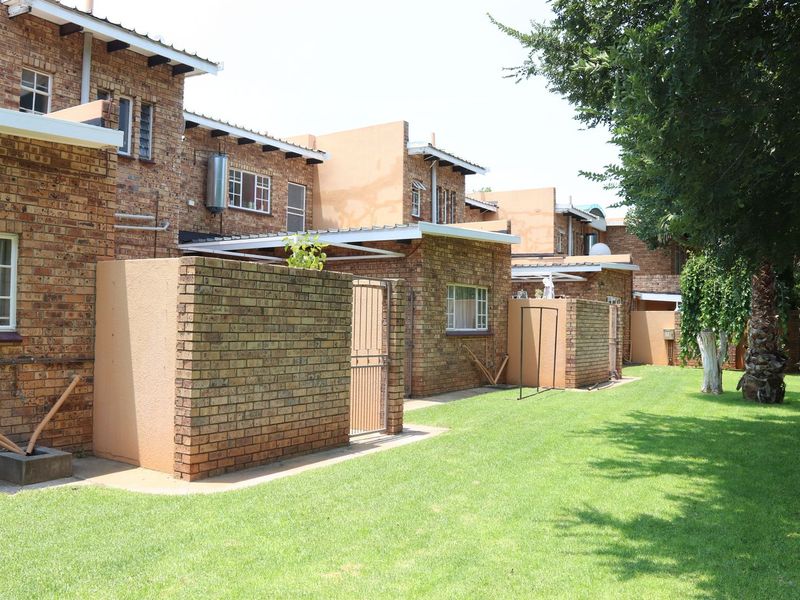 Rear view of a commercial townhouse complex featuring face brick construction, metal roofing, and private enclosed courtyard areas with established lawn.