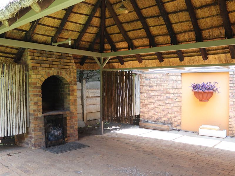 Covered outdoor patio area featuring a traditional thatched roof, brick paving, and a built-in brick braai, ideal for outdoor entertaining.