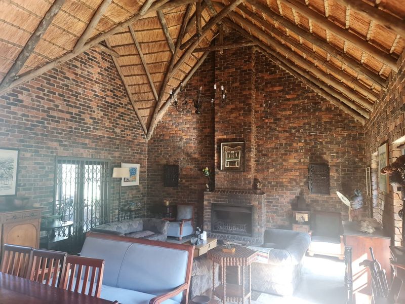 Spacious living room featuring a high vaulted thatch ceiling with exposed timber rafters and a prominent built-in brick fireplace.