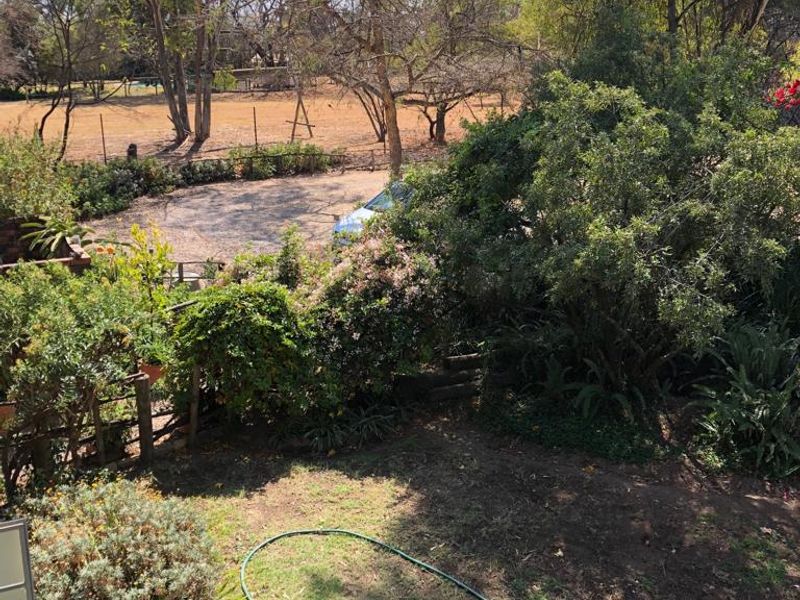 An elevated view overlooking a private garden with mature trees and shrubs, extending towards a rural landscape beyond the property boundary.