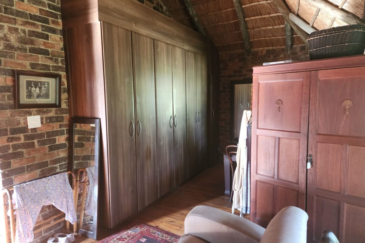 A rustic bedroom featuring exposed brick walls, a traditional thatched roof, timber flooring, and extensive built-in cupboard storage.