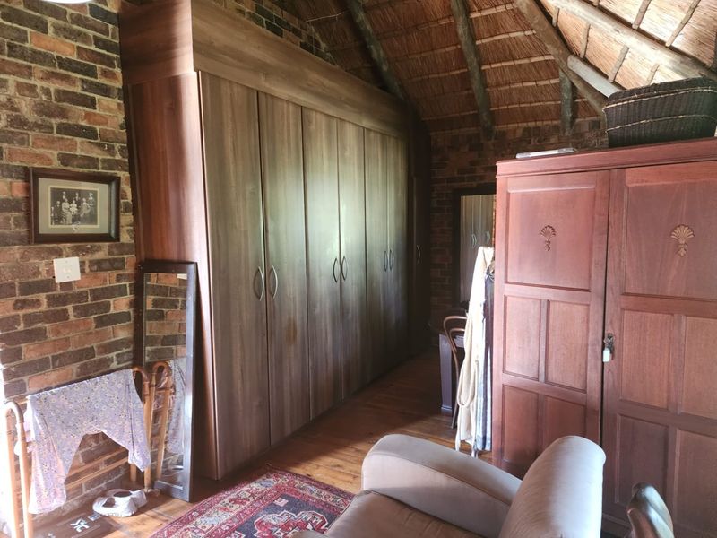 A rustic bedroom featuring exposed brick walls, a traditional thatched roof, timber flooring, and extensive built-in cupboard storage.