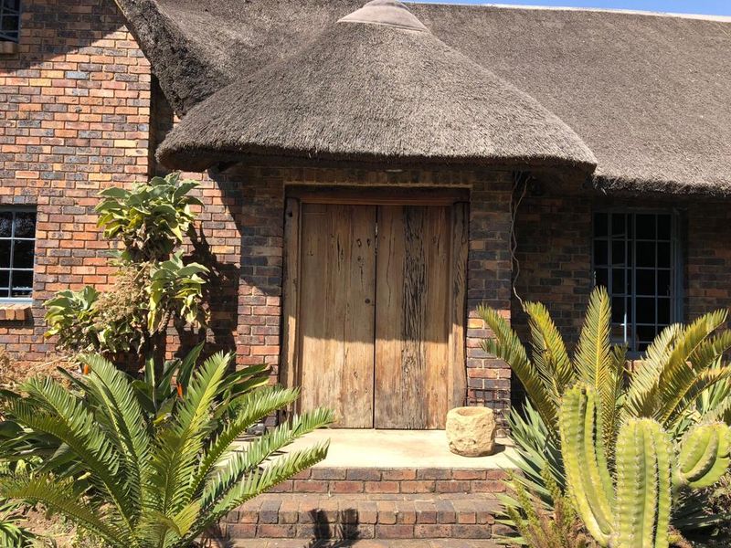 Front entrance of a farm-style property featuring a traditional thatched roof, face brick exterior, and rustic timber double doors.