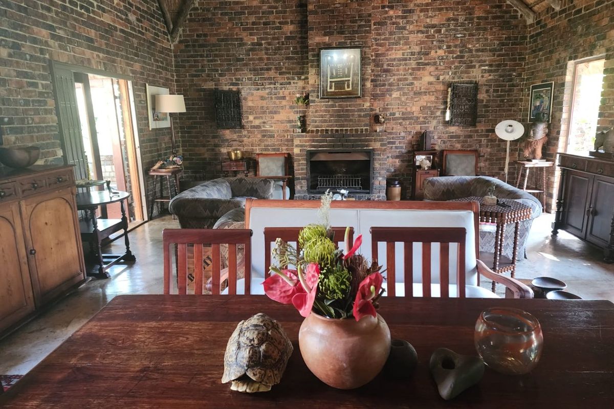 Spacious living room featuring rustic exposed brick walls, a high vaulted thatched ceiling, and a central built-in fireplace, creating a warm and traditional atmosphere.