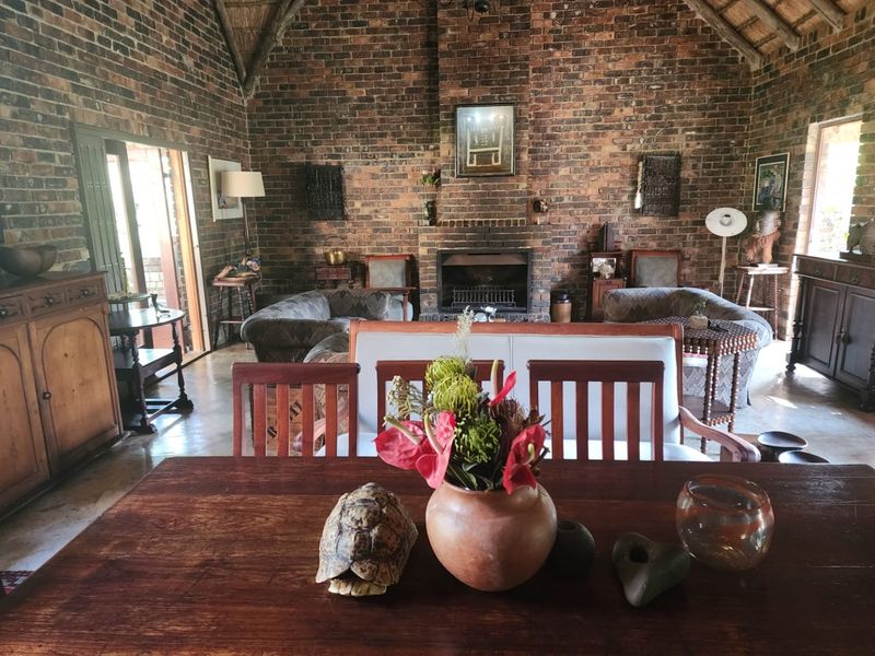 Spacious living room featuring rustic exposed brick walls, a high vaulted thatched ceiling, and a central built-in fireplace, creating a warm and traditional atmosphere.