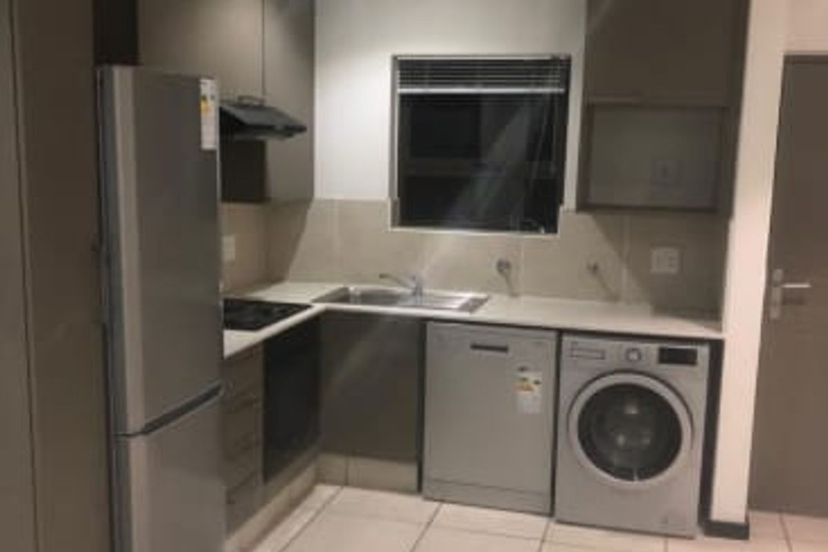 Modern kitchen featuring dark cabinetry, tiled flooring, built-in oven, hob, extractor fan, and integrated space for laundry and dishwashing appliances.
