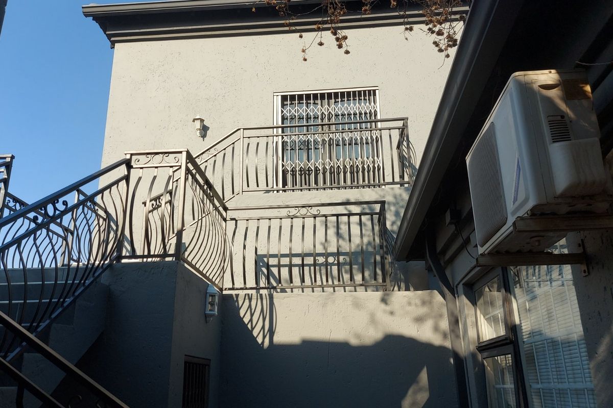 Rear exterior view featuring a wrought iron staircase, security gate, and wall-mounted air conditioning unit on a multi-level commercial building facade.
