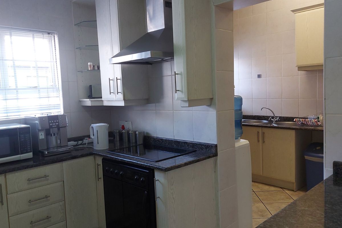 A functional kitchen featuring built-in cabinetry, granite countertops, an electric hob with extractor fan, and an adjoining scullery area with a double sink.
