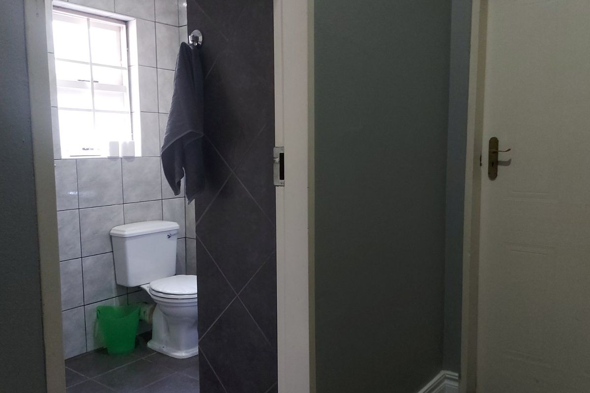 A functional bathroom featuring tiled walls and flooring, with a standard toilet and window for natural light.