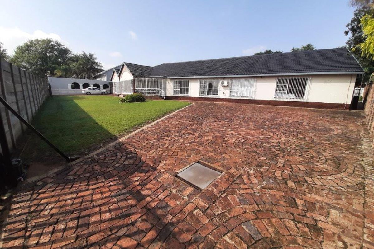 Spacious rear exterior featuring a large brick-paved driveway, well-maintained lawn, and a secure boundary wall.