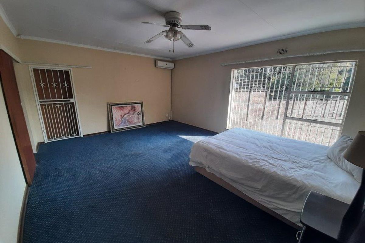 Spacious bedroom featuring a ceiling fan, split-system air conditioning, and security bars on the windows. The room offers a functional layout with carpeted flooring.