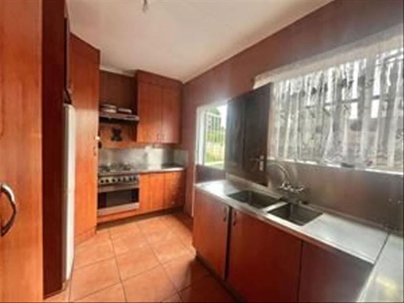 A functional kitchen featuring wooden cabinetry, a stainless steel sink, built-in oven, and hob with tiled flooring.