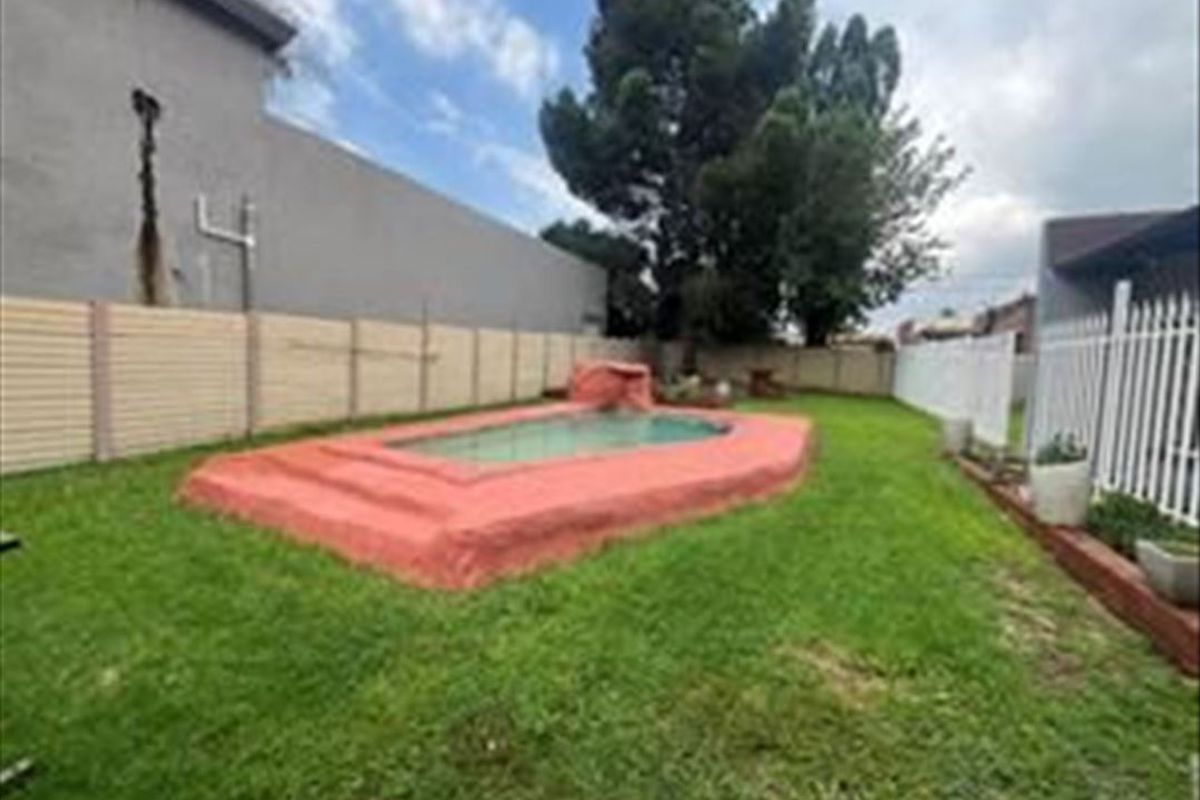 Rear garden area featuring a raised swimming pool, enclosed by precast concrete and metal fencing, with visible structural cracking on the adjacent exterior wall.