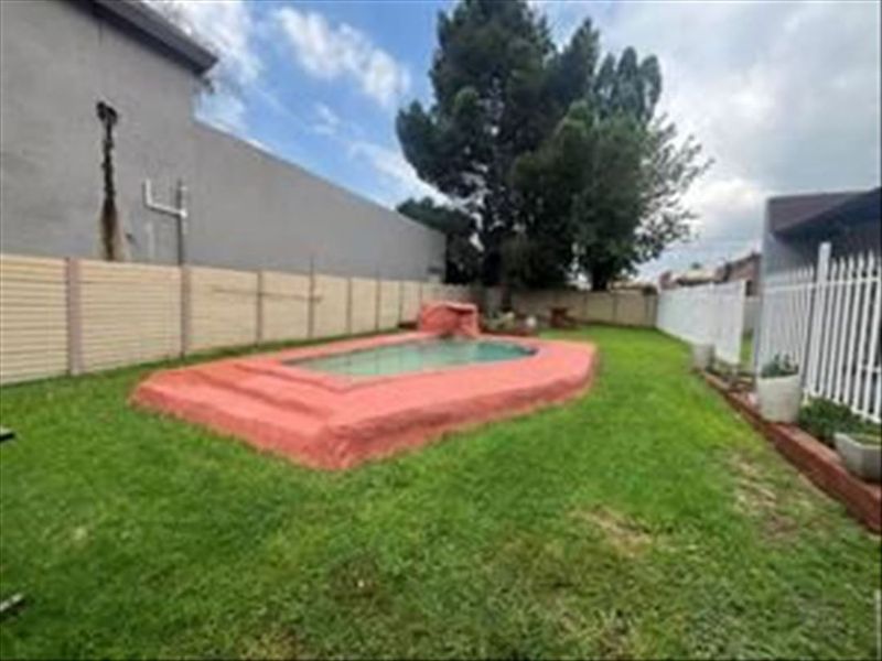 Rear garden area featuring a raised swimming pool, enclosed by precast concrete and metal fencing, with visible structural cracking on the adjacent exterior wall.