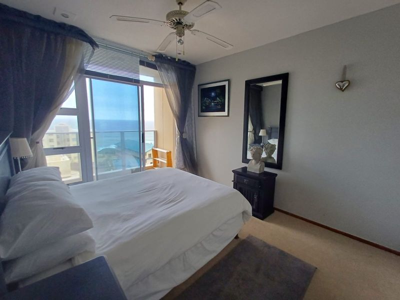 A bedroom featuring a ceiling fan and a sliding glass door that opens onto a balcony with ocean views.