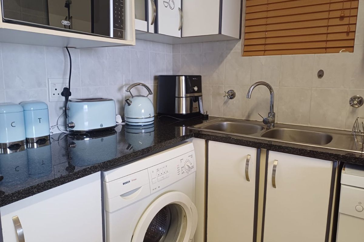 A functional kitchen featuring granite countertops, a double basin sink, tiled backsplash, and integrated space for a washing machine.
