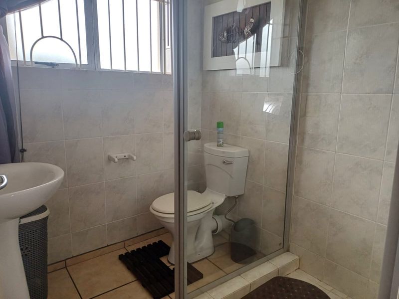 A functional bathroom featuring a pedestal basin, toilet, and a glass-enclosed shower with neutral ceramic tiling throughout.