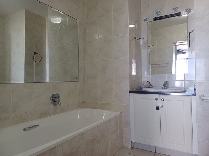 A functional bathroom featuring a built-in bathtub, vanity cabinet with basin, and neutral wall tiling throughout.