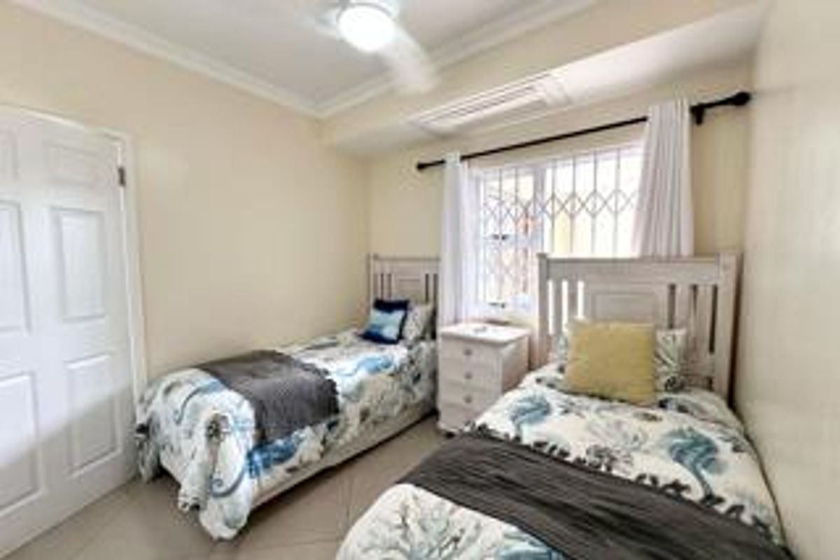 A functional bedroom featuring tiled flooring, a ceiling fan, and a window fitted with security bars.