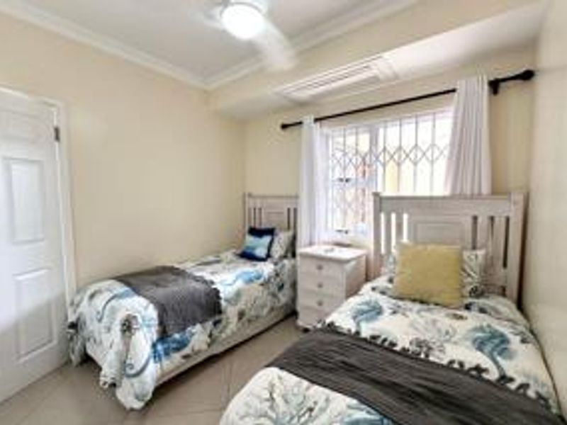 A functional bedroom featuring tiled flooring, a ceiling fan, and a window fitted with security bars.