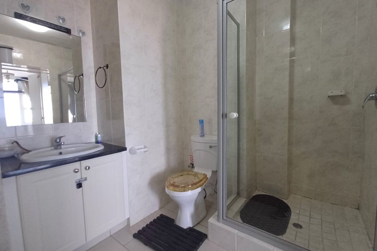 A functional bathroom featuring a vanity cabinet with integrated basin, a glass-enclosed shower, and tiled finishes throughout.