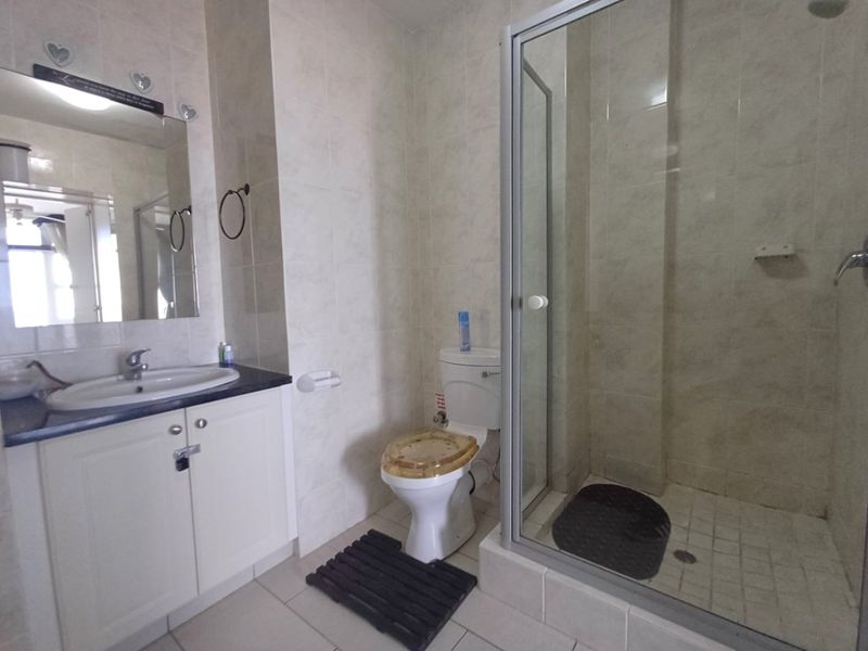 A functional bathroom featuring a vanity cabinet with integrated basin, a glass-enclosed shower, and tiled finishes throughout.