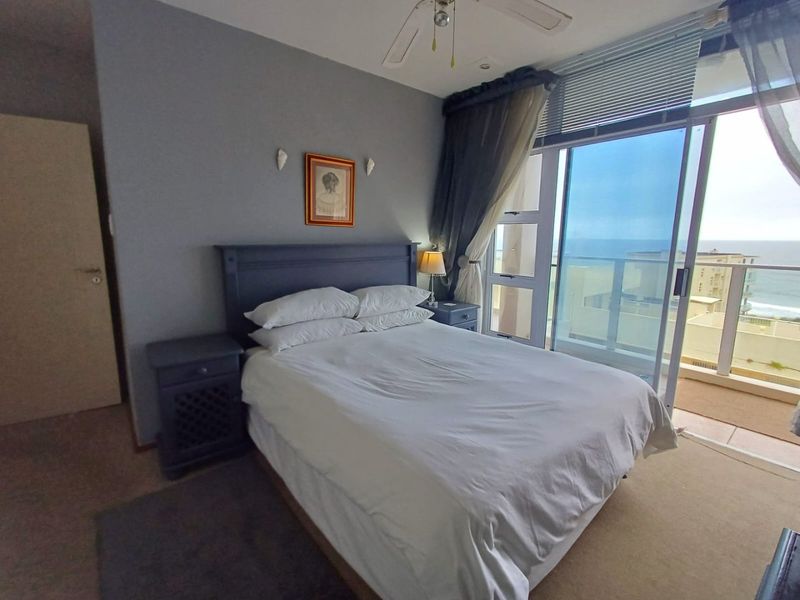 A comfortable bedroom featuring carpeted flooring, a ceiling fan, and large sliding glass doors that provide direct access to a balcony with ocean views.