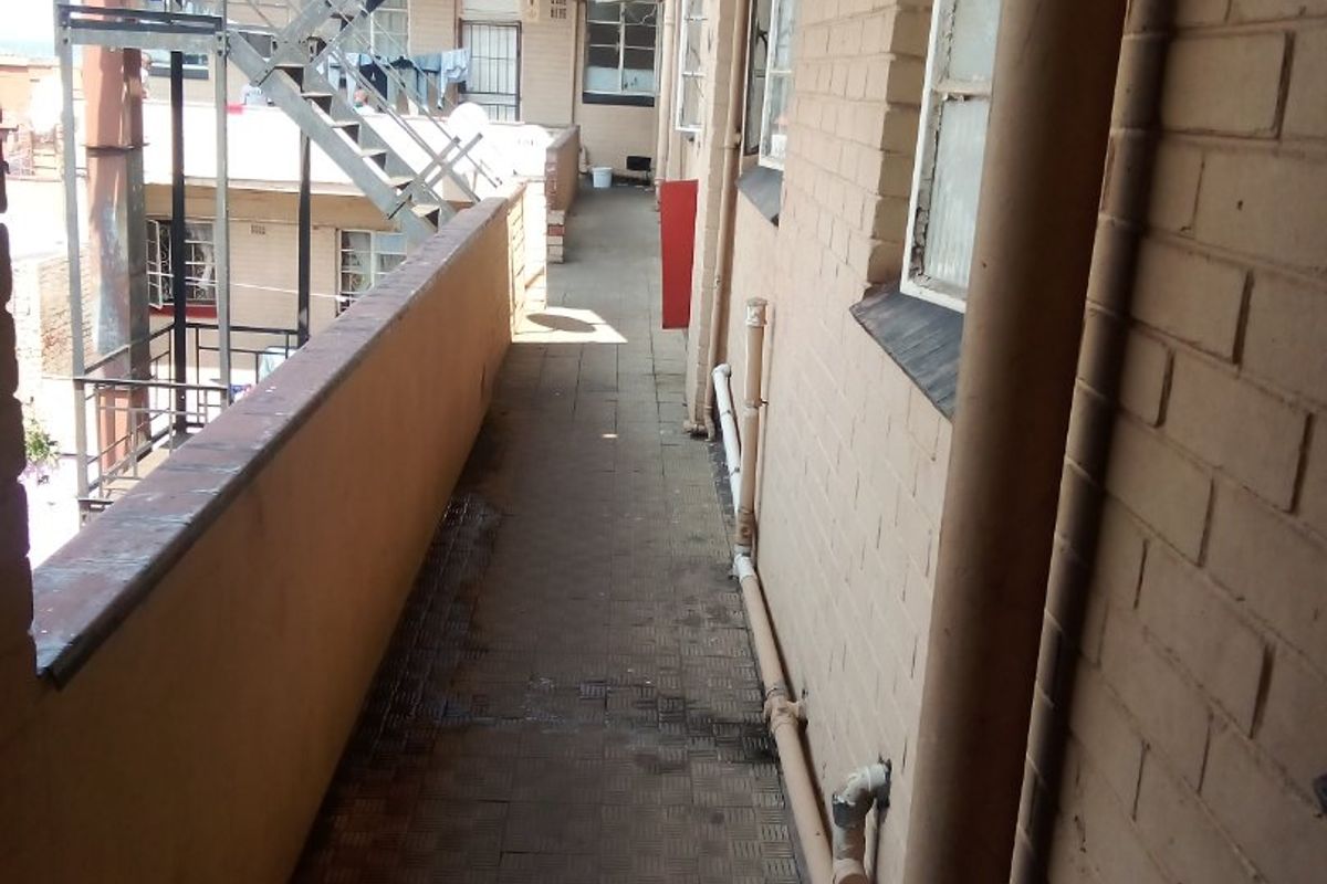 An exterior walkway or balcony area featuring brick walls, tiled flooring, and an external metal staircase providing access to the commercial building levels.