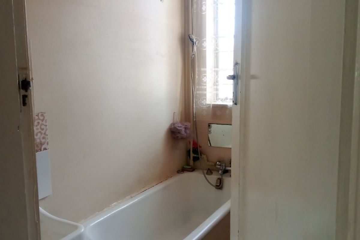 A compact bathroom featuring a built-in bathtub and wall-mounted basin, requiring cosmetic updates to modernize the space.