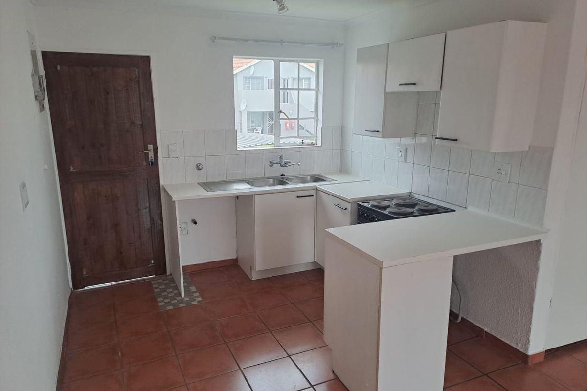 A functional kitchen featuring white cabinetry, a built-in stove, double sink, and tiled flooring with direct access to an exterior door.