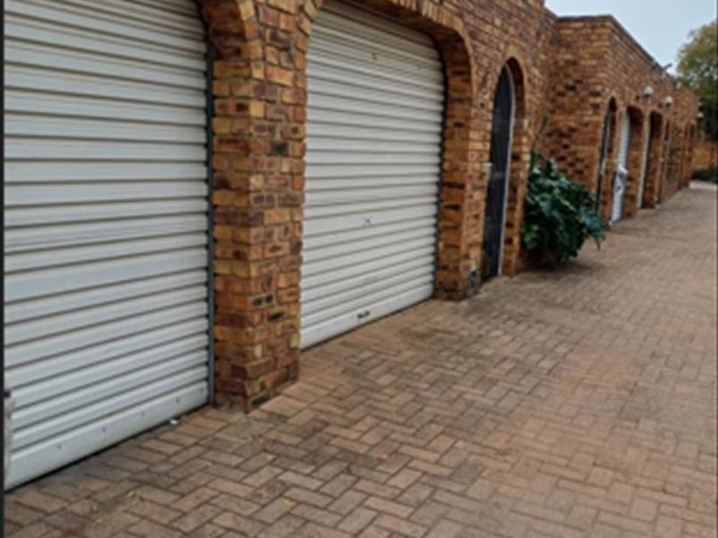 A row of garages featuring face-brick construction with arched openings and secure roller shutter doors, set along a paved driveway.