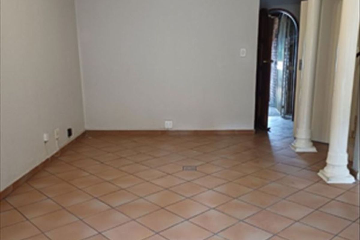 An empty living room featuring ceramic tile flooring, decorative columns, and a ceiling fan, offering a blank canvas for interior design.