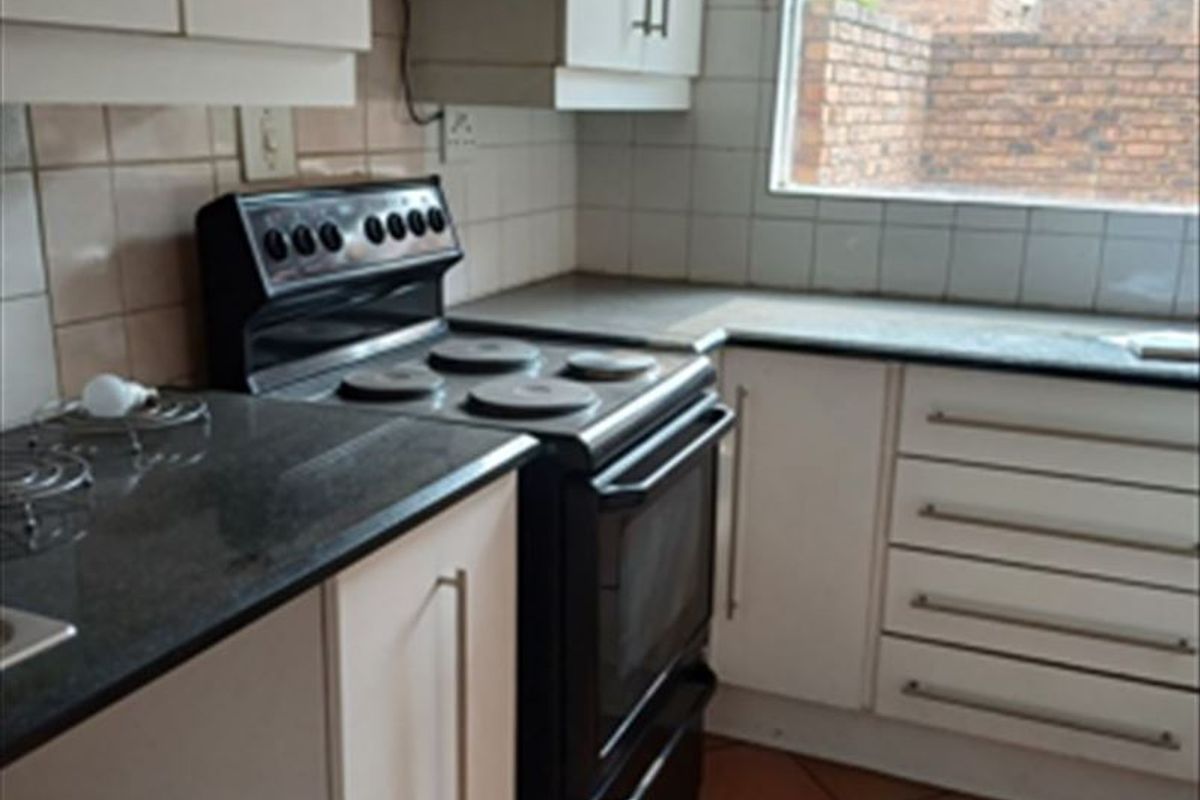 Functional kitchen featuring white cabinetry, dark stone countertops, tiled backsplash, and ceramic flooring, offering a practical layout for daily meal preparation.