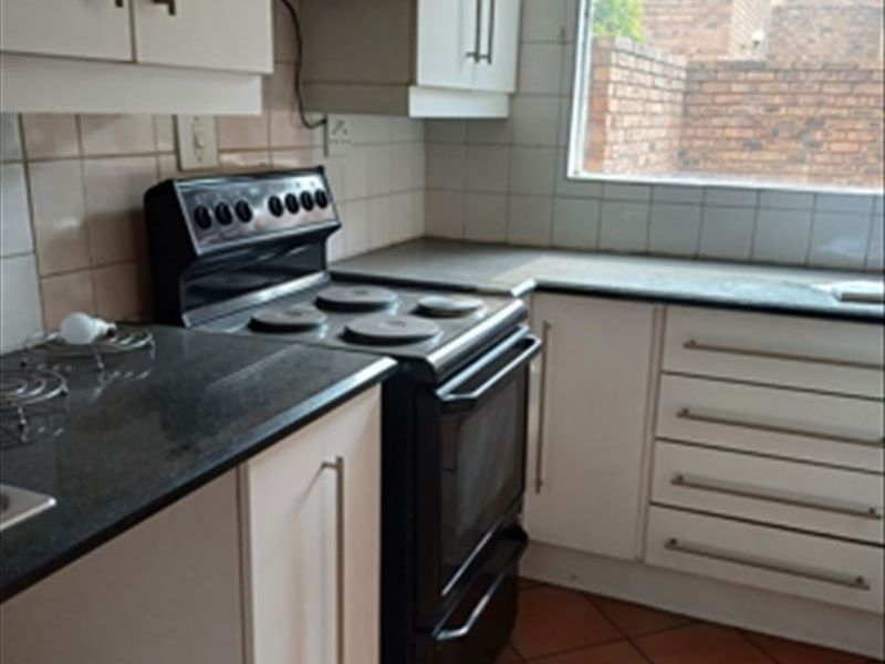 Functional kitchen featuring white cabinetry, dark stone countertops, tiled backsplash, and ceramic flooring, offering a practical layout for daily meal preparation.