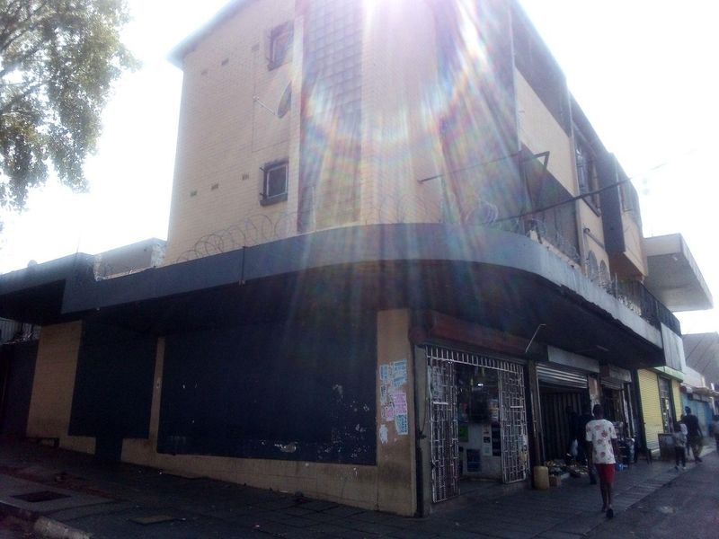A commercial building exterior featuring a corner facade with roller shutter doors, security gates, and razor wire fencing along the upper levels.